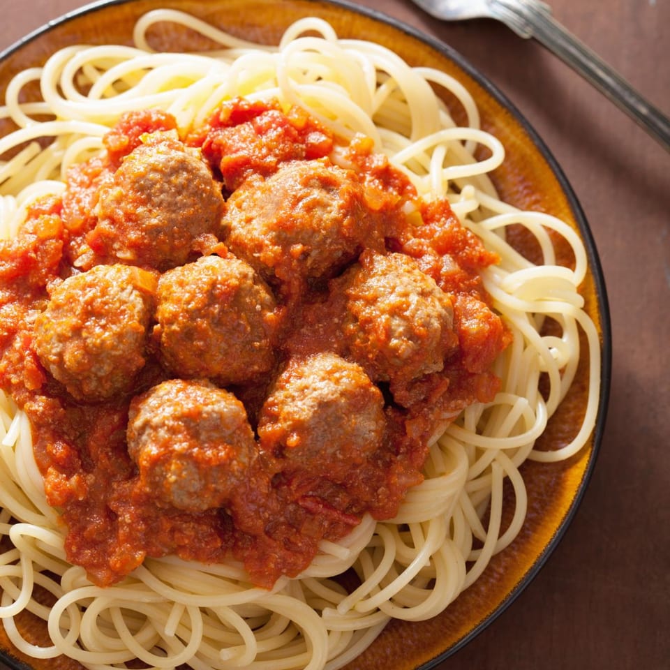 Spaghetti with meatballs and rich tomato sauce on a brown plate, with a fork nearby.