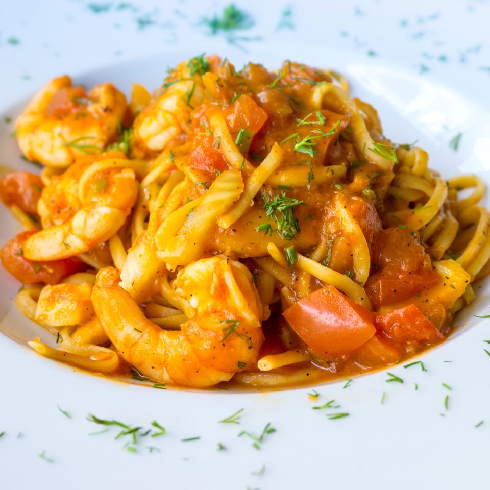 Close-up of shrimp pasta with tomato sauce and fresh herbs on a white plate.