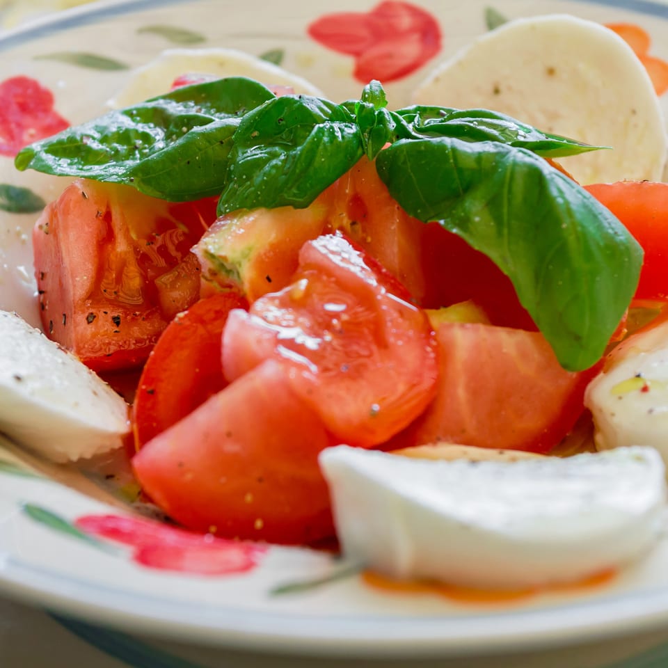 Caprese salad with fresh mozzarella, sliced tomatoes, and basil leaves on a decorative plate.